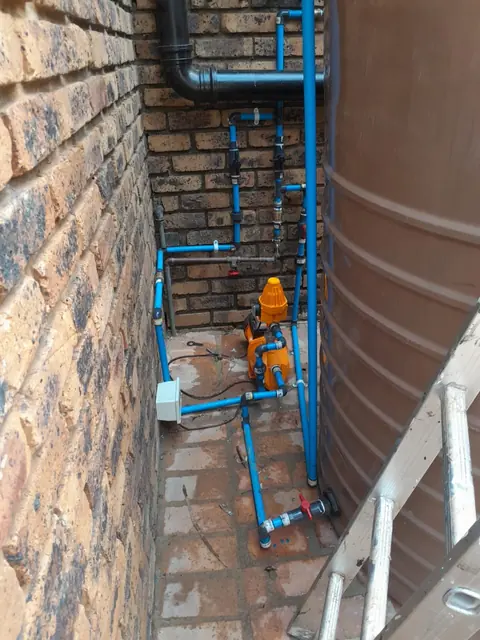 Outdoor pressure pump and plumbing installation against an exterior wall