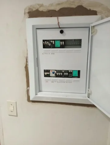 Newly installed white distribution board with circuit breakers, set into a wall still being patched