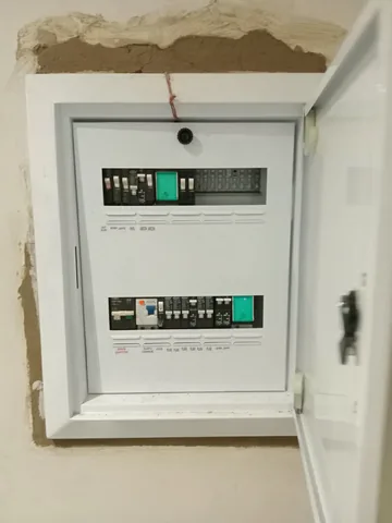 Flush-mounted white distribution board with organised breakers in an unfinished renovation wall