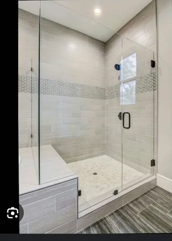 Walk-in glass shower with mosaic accent strip, pebble floor and matte black hardware