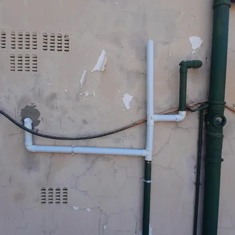 New white PVC conduit strapped to an exterior wall with metal brackets