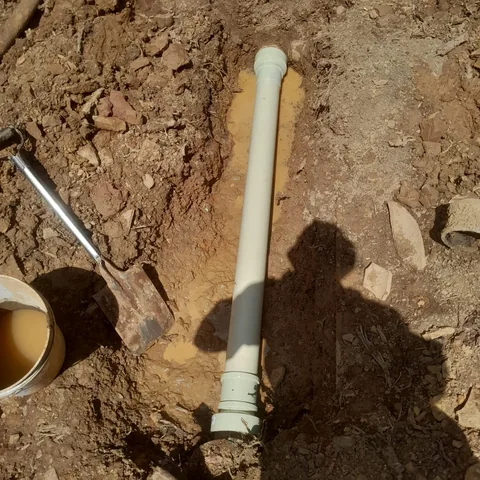 PVC pipe laid in a freshly dug trench with a shovel and bucket at a work site