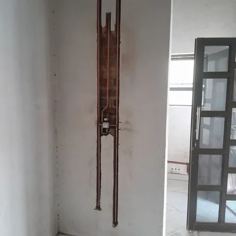 Copper pipes installed in a vertical chase cut through plaster into brickwork