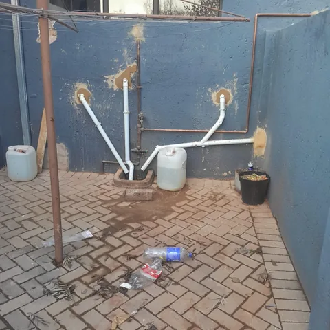 Exterior PVC and copper pipework on a blue wall draining to a brick-paved gully