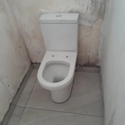 White ceramic toilet installed in a tiled bathroom still under renovation