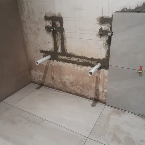 Plumbing rough-in pipes in mortar and new floor tiles during a bathroom renovation