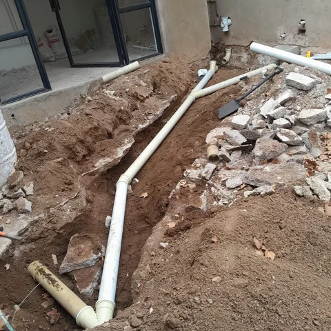 Underground PVC drainage pipes and junctions laid in an excavated trench beside a house