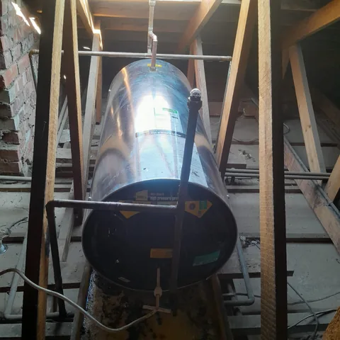 Horizontal stainless-steel geyser installed in a roof space with copper and plastic pipework